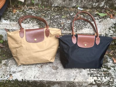 une paire de sacs à main Longchamp en toile et cuir posés sur des marches en pierre