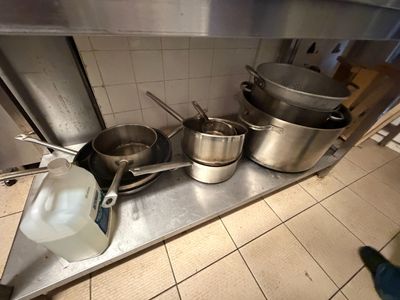 Des casseroles et des poêles sont alignées sur une étagère métallique dans une cuisine