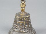 brass bell with a figure on top of it on a gray surface
