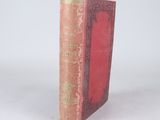 an old book with a red cover sitting on a white surface