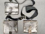 deux porte-monnaie en cuir argenté avec une lanière noire, posés sur un fond gris