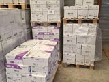 Plusieurs piles de cartons sont empilées sur des palettes dans un entrepôt
