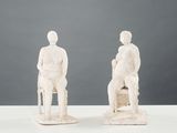 pair of white sculptures of a man and a woman sitting on a chair