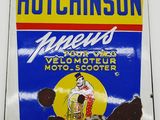 une vieille enseigne en tôle faisant la promotion de l'huile moteur Hutchinson, accrochée à un mur blanc