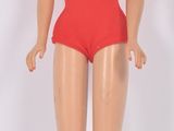 une poupée Barbie en maillot de bain rouge, debout sur une surface blanche