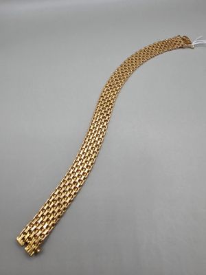une image représentant un bracelet en or posé sur une surface grise
