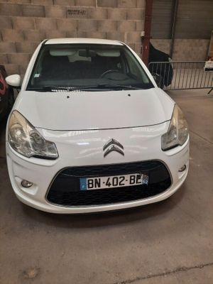 La voiture blanche est garée dans le garage, à côté d'autres voitures.