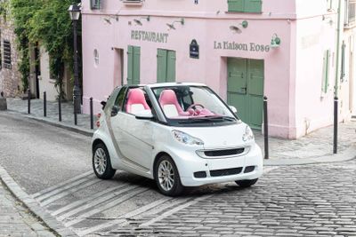 a small white car driving down a cobblestone street