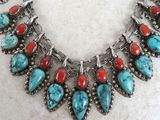 a close up of a necklace with turquoise and red stones