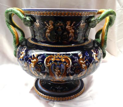 un grand vase bleu muni d'une anse verte, posé sur un socle