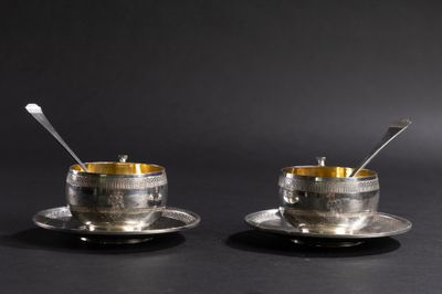 deux tasses et soucoupes en argent avec leurs cuillères, posées sur une surface noire