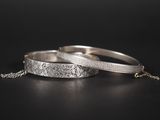 une paire de bracelets en argent posés sur une surface noire