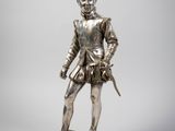 une statue en argent représentant un homme armé d'une épée, posée sur un socle en bois