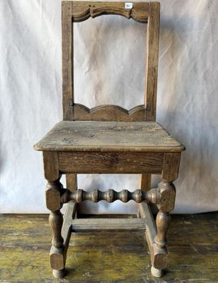 une vieille chaise en bois posée sur un parquet, près d'un mur blanc