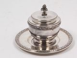 une assiette en argent avec un couvercle en argent, posée sur une soucoupe