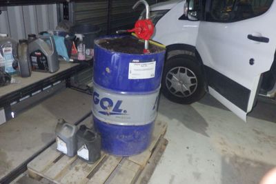 un fût bleu posé sur une palette à côté d'une camionnette blanche