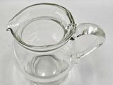 clear glass pitcher with a handle on a white surface