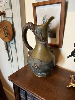 a bronze pitcher sitting on top of a book shelf