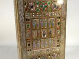 un livre en or richement décoré, sur lequel figure l'image d'une femme entourée de bijoux et de pierres précieuses