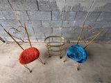 trois chaises en métal avec des coussins rouges, bleus et orange sont assises devant un mur de briques