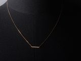 a gold necklace with a bar pendant on a mannequin neck