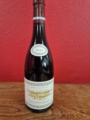 La bouteille de vin est posée sur la table, devant un mur rouge.