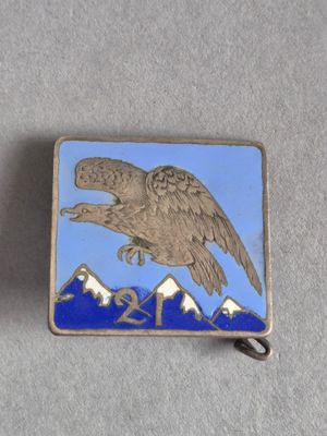 une image représentant une broche en forme d'aigle argenté et bleu, avec des montagnes en arrière-plan