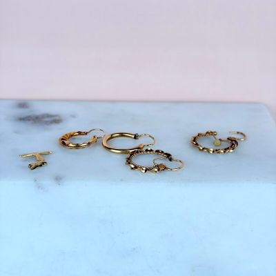 three pairs of gold hoop earrings sitting on a marble slab