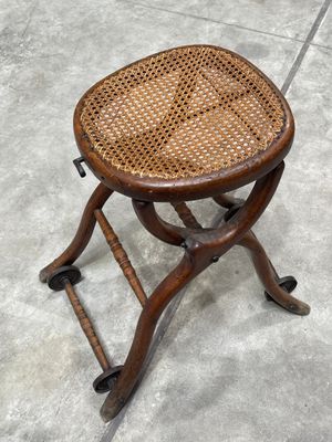 un vieux tabouret en bois avec une assise en osier, posé sur un sol en béton