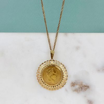 une photo d'un collier avec une pièce d'or posé sur une surface en marbre