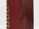 an old book with a red cover sitting on top of a white table
