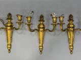a set of five brass wall mounted sconces on a white wall