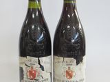 two bottles of red wine sitting next to each other on a white surface
