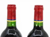 two bottles of red wine sitting next to each other on a white surface