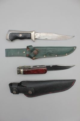 Plusieurs couteaux sont alignés sur une surface blanche, accompagnés d'un étui en cuir.