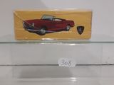 a red toy car on a glass shelf with a yellow box