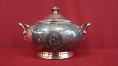 an antique silverplated bowl with a lid and handles on a red background