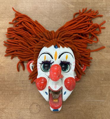 un masque de clown aux cheveux roux posé sur une table en bois