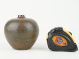 a brown vase and a tape measure on a white surface