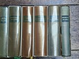 six old books are lined up on a wooden table