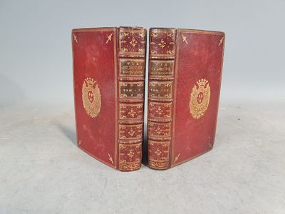 deux livres rouges ornés de motifs dorés, posés sur une surface blanche