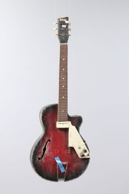 an old red guitar hanging from a string on a white wall