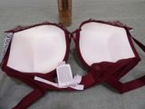 pair of red and white bras sitting on top of a bed next to a bottle of liquid