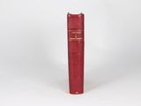 an old red book sitting on top of a table next to a white wall