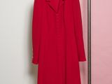 Le manteau rouge est suspendu à un cintre devant un mur rose.