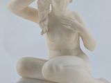 a white statue of a woman sitting on top of a rock