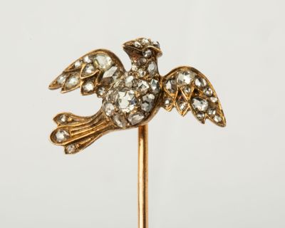 une image représentant une broche en forme d'oiseau, en or et diamants, fixée sur une tige