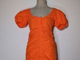 une robe orange posée sur un mannequin, devant un mur blanc