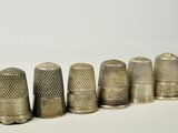 six antique thimbles lined up in a row on a white surface