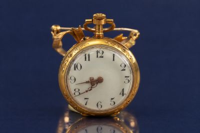 une montre de poche en or posée sur une table, sur un fond bleu